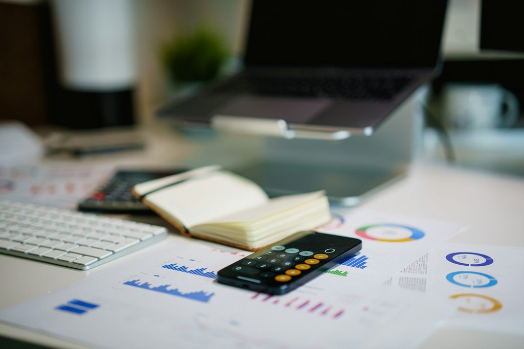 A desk setup featuring a laptop, a calculator, colorful graphs, and a calculator over financial milestone documents.